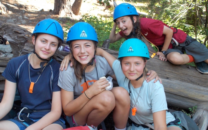 a group of outward bound students wearing blue helmets pose for a photo on a rock climbing course